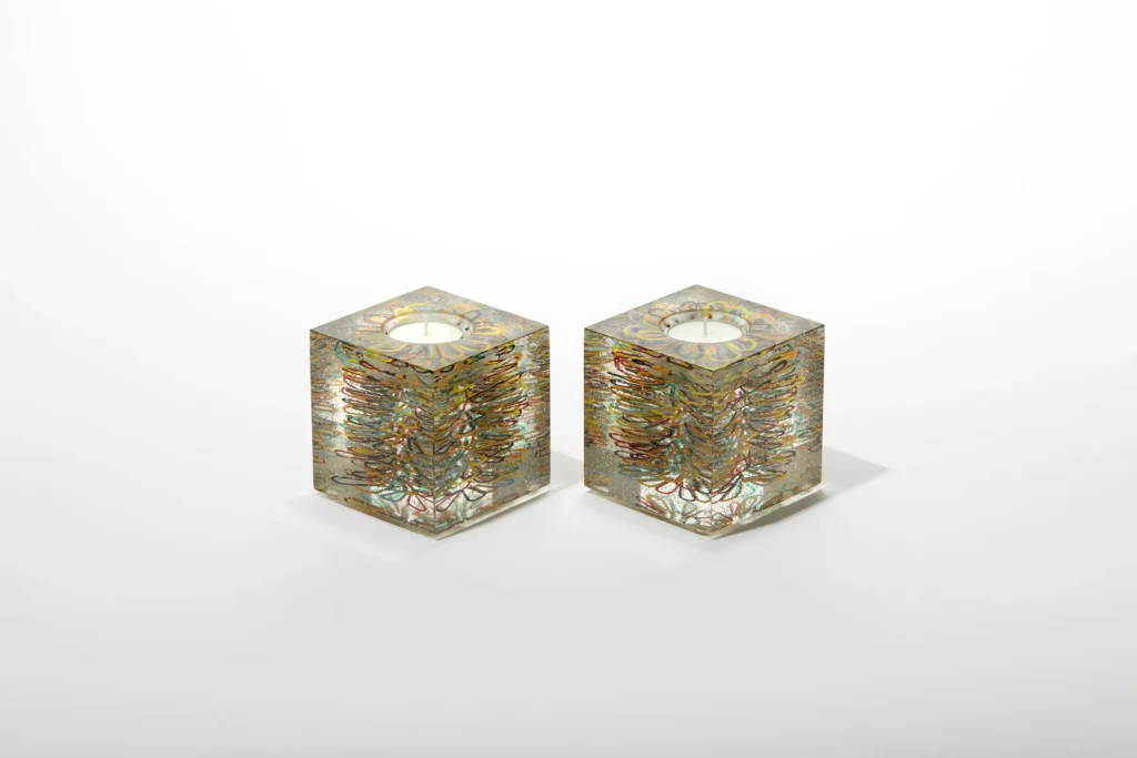 A pair of small, clear glass candle holders with a delicate, layered golden floral pattern
