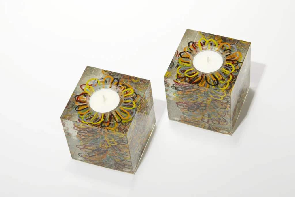 A pair of small, clear glass candle holders with a delicate, layered golden floral pattern