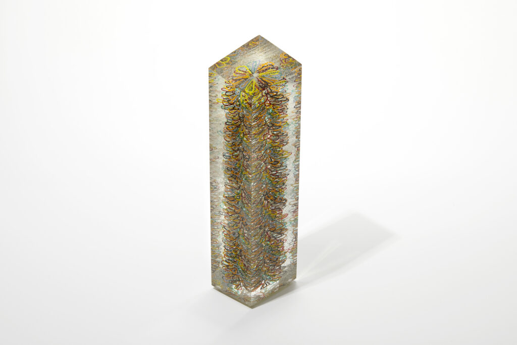 A tall, multi-faceted glass obelisk titled 'Stack 42', filled with a dense, colourful, spiraling linear pattern.