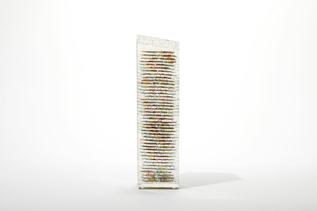 A side view of the 'Stack 42' obelisk, showing its vertically stacked layers of colourful glass threads.