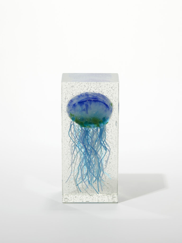 A tall, clear glass block sculpture with a vibrant blue jellyfish fused inside.