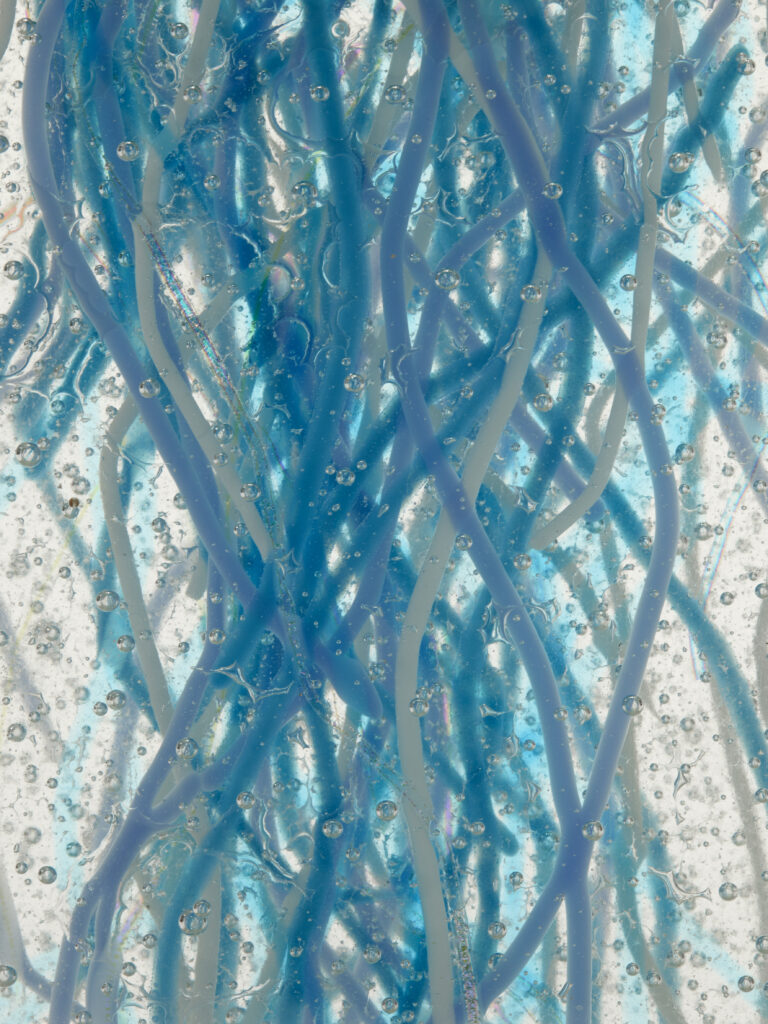A close-up of blue, wavy, thread-like glass pieces fused together to create a chaotic, watery pattern.