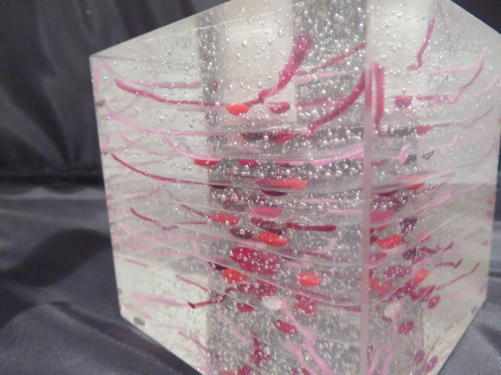 A close-up of a clear, block-shaped candle holder with vibrant red, root-like patterns fused within the glass.