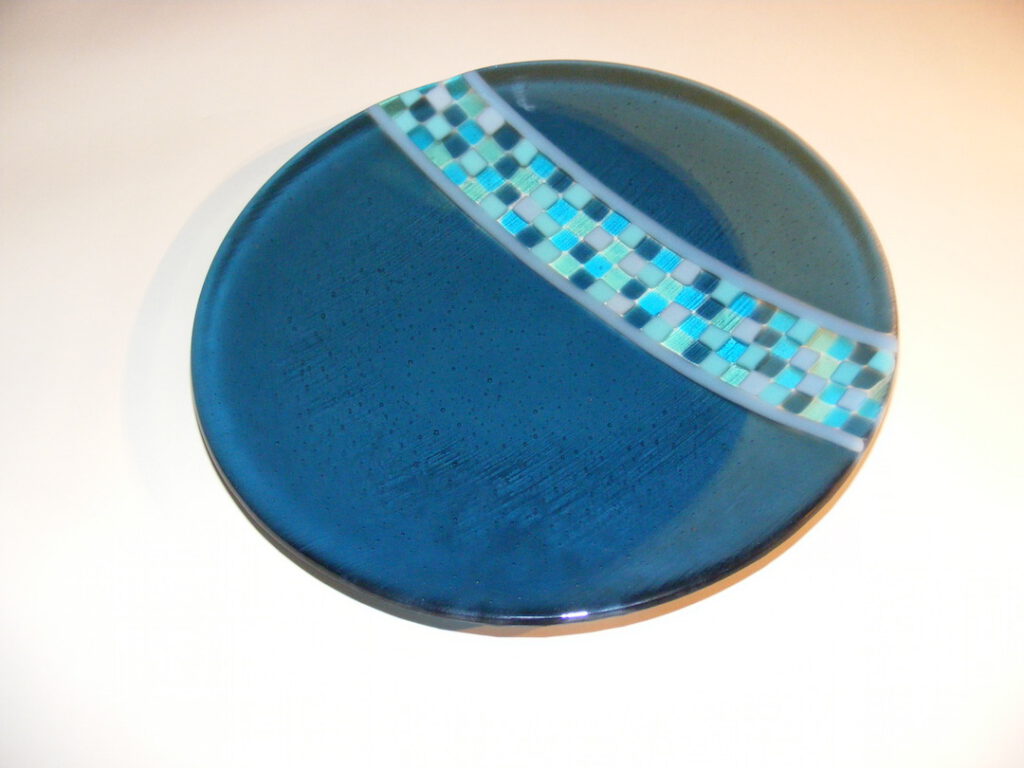 A round, dark blue glass dish with a diagonal band of light blue checkered patterns across its surface.