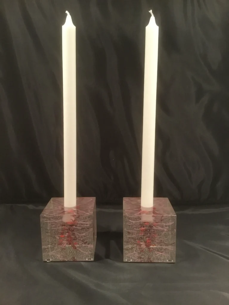 A front view of a pair of square glass candle holders, showing their red internal designs and inserted white candles.