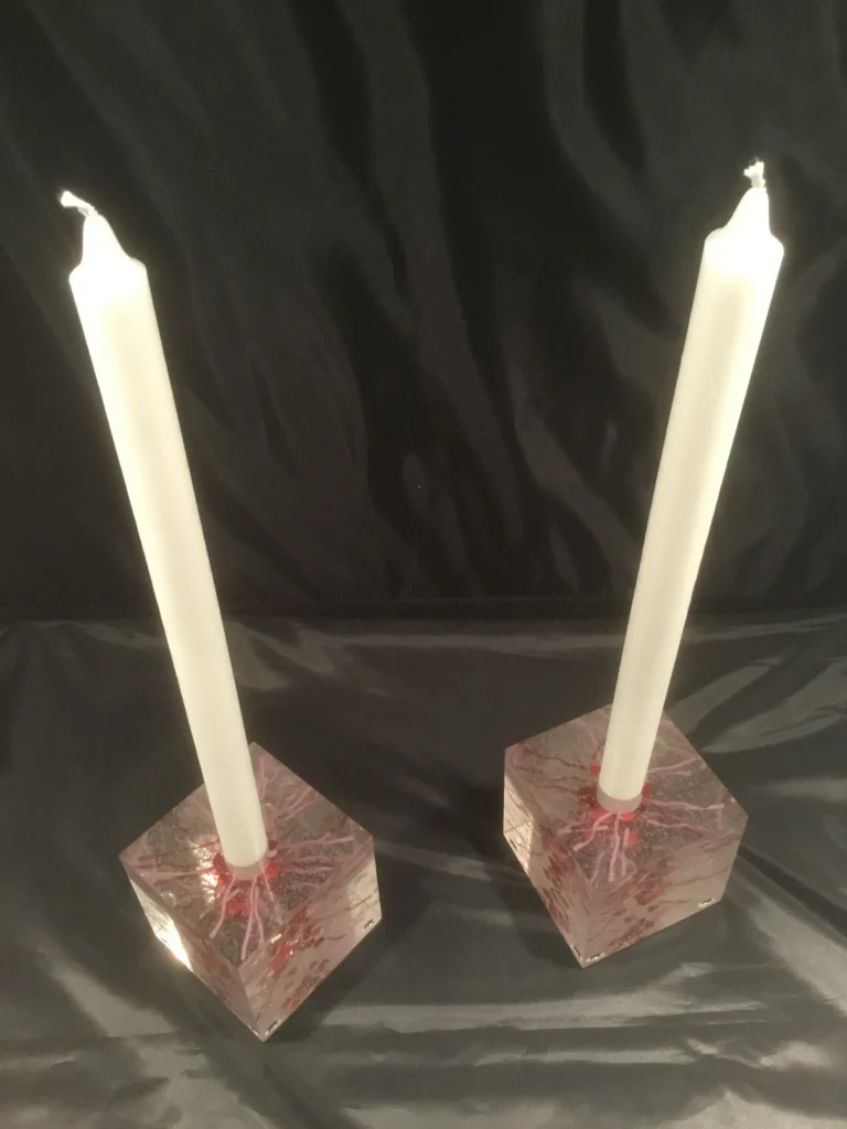 Two angled, multi-faceted glass candle holders with red internal patterns, each holding a white candle.