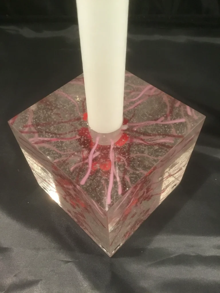 A top-down view of a clear glass candle holder with a candle inserted, showing the chaotic red internal design.
