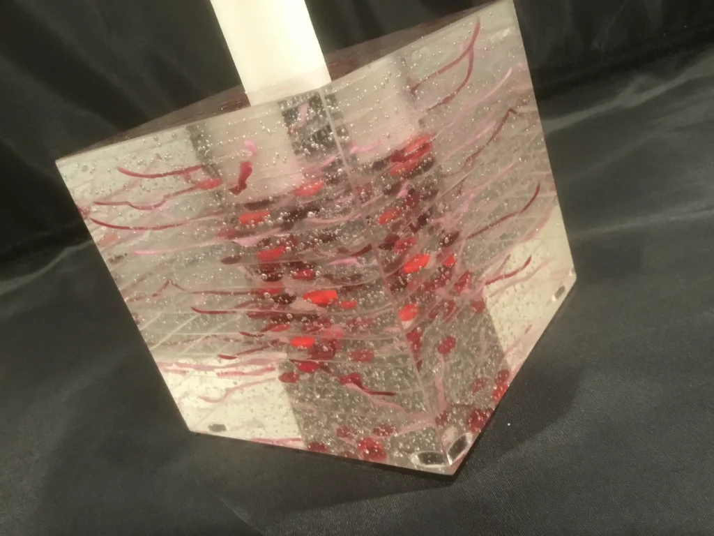 A detailed side view of a glass candle holder, highlighting the intricate red and silver layered patterns.