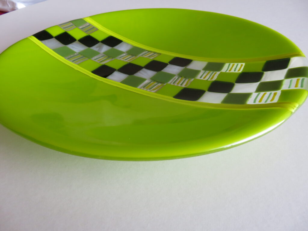A bright green curved dish featuring a curved mosaic band of grey and white checkered squares.