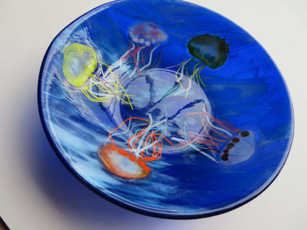 A blue glass disc bowl with a fused white octopus and other sea life patterns.