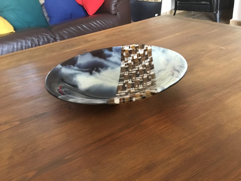 A dish with a dynamic black and white mosaic pattern, displayed on a wooden table.