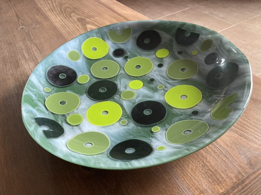 A light green disc bowl viewed from above, decorated with a playful pattern of black, white, and green circles.