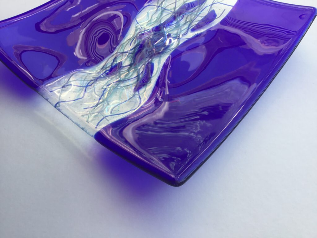 A deep purple glass piece, showing a highly polished surface with a swirling, stream-like pattern.