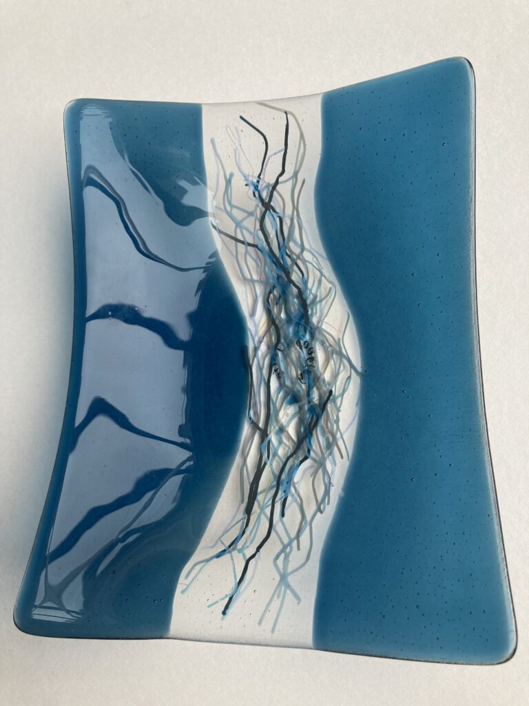 A close-up of a blue glass dish, highlighting the flowing white and black patterns in the center.