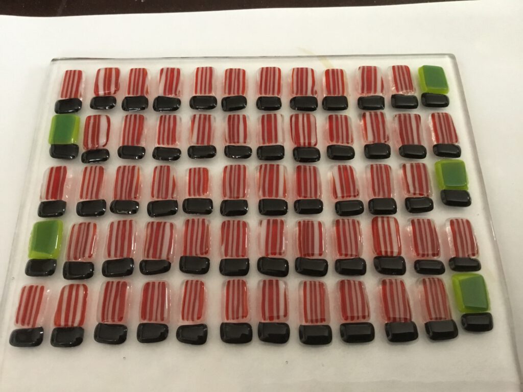 A grid of tiny red and white striped glass shirts and black shorts laid out for assembly on a flat surface.