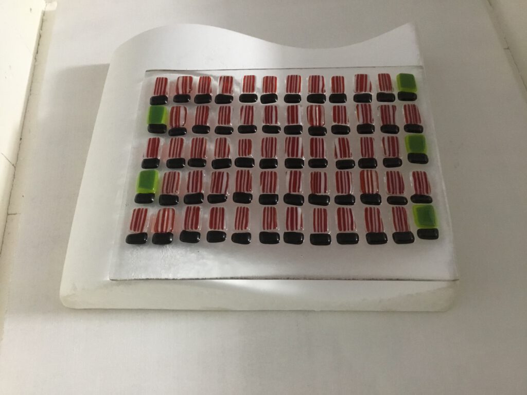 The red and white glass football shirts carefully arranged on a sheet of clear glass before being fused into the wave.