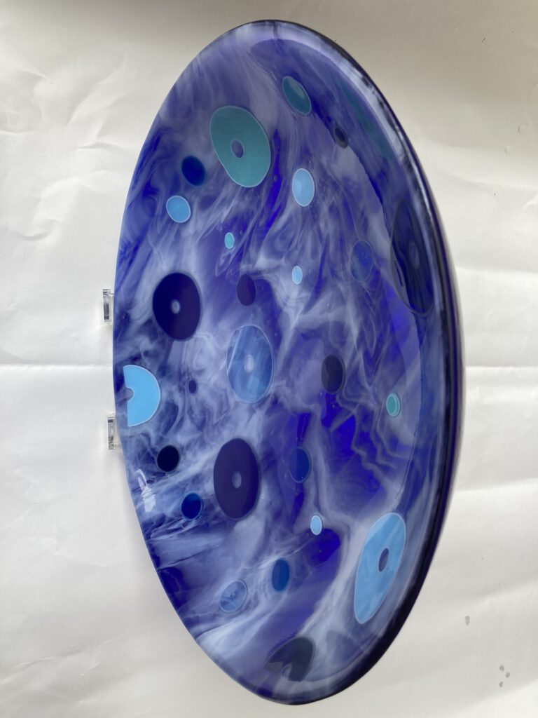 A deep blue swirled glass disc bowl seen from the side, with various blue and light blue circular patterns.