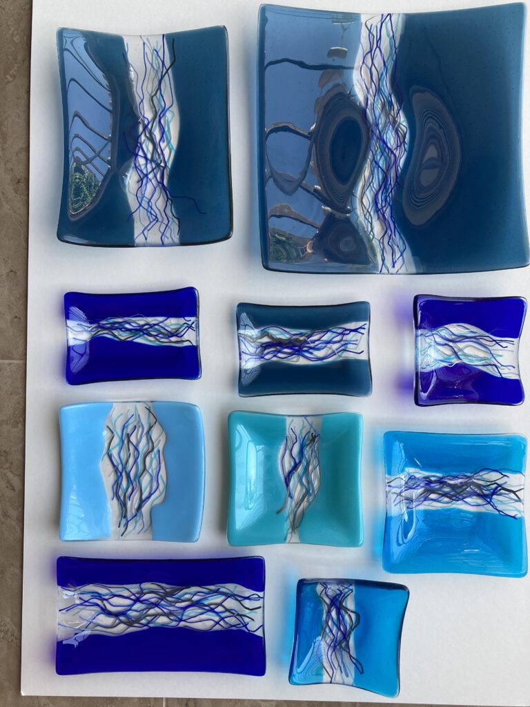 A collection of small, rectangular glass dishes in various blues, each with a unique river-like design.