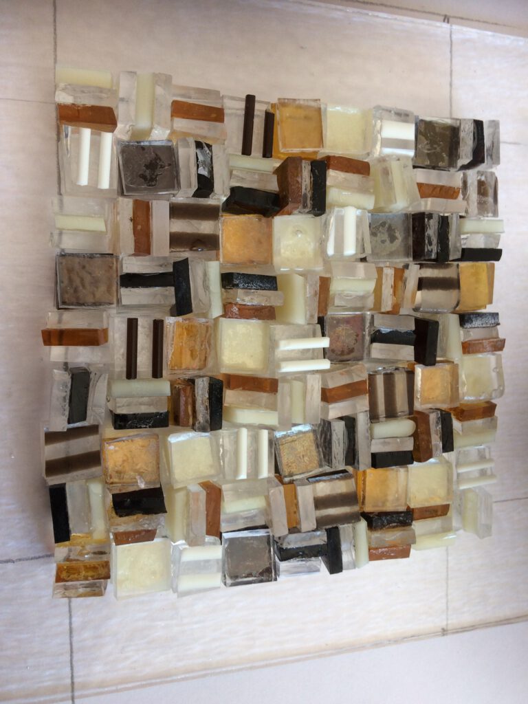 A square wall panel mosaic made from textured, earthy-toned glass blocks with black lines between them.