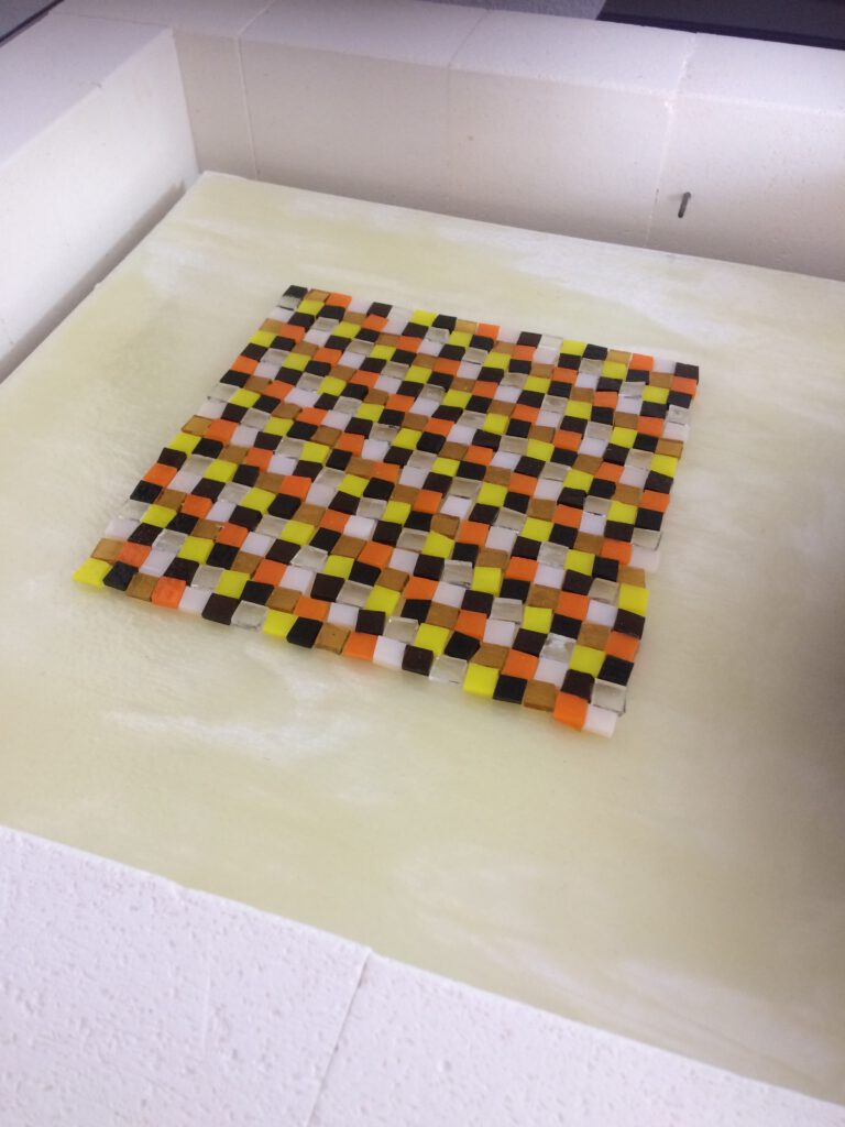 A colourful mosaic piece with a checkered pattern of orange, yellow, and red squares laid out for fusing.
