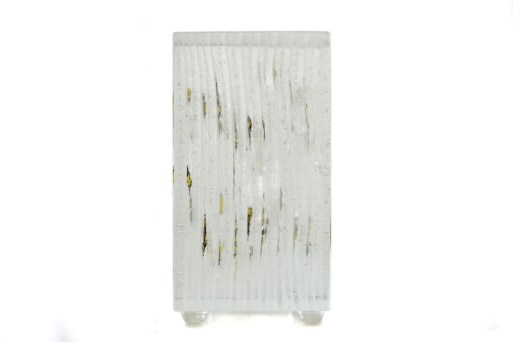 A side view of the sculptural glass block, showing a ribbed texture and the fused bees as thin vertical streaks.