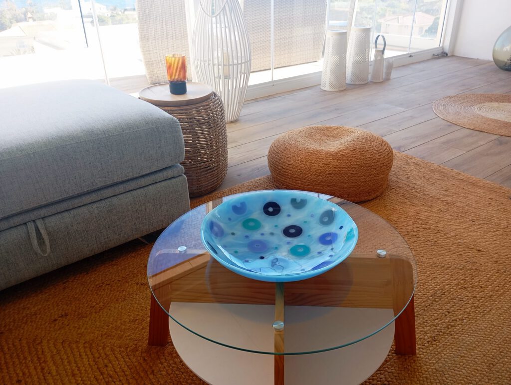 A light blue polka-dot glass disc bowl displayed on a coffee table in a contemporary living room setting.
