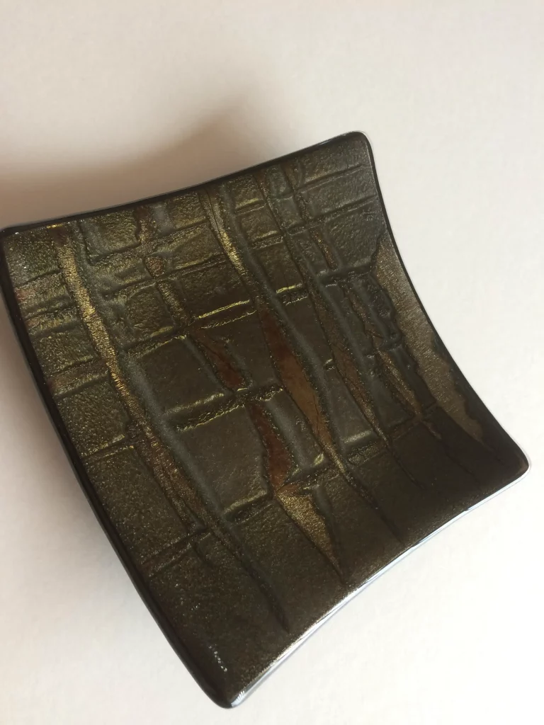 A small, deep blue fused glass dish with gently curved sides. Five white daisy flowers with yellow centers are fused onto its surface, arranged to spread across the dish.